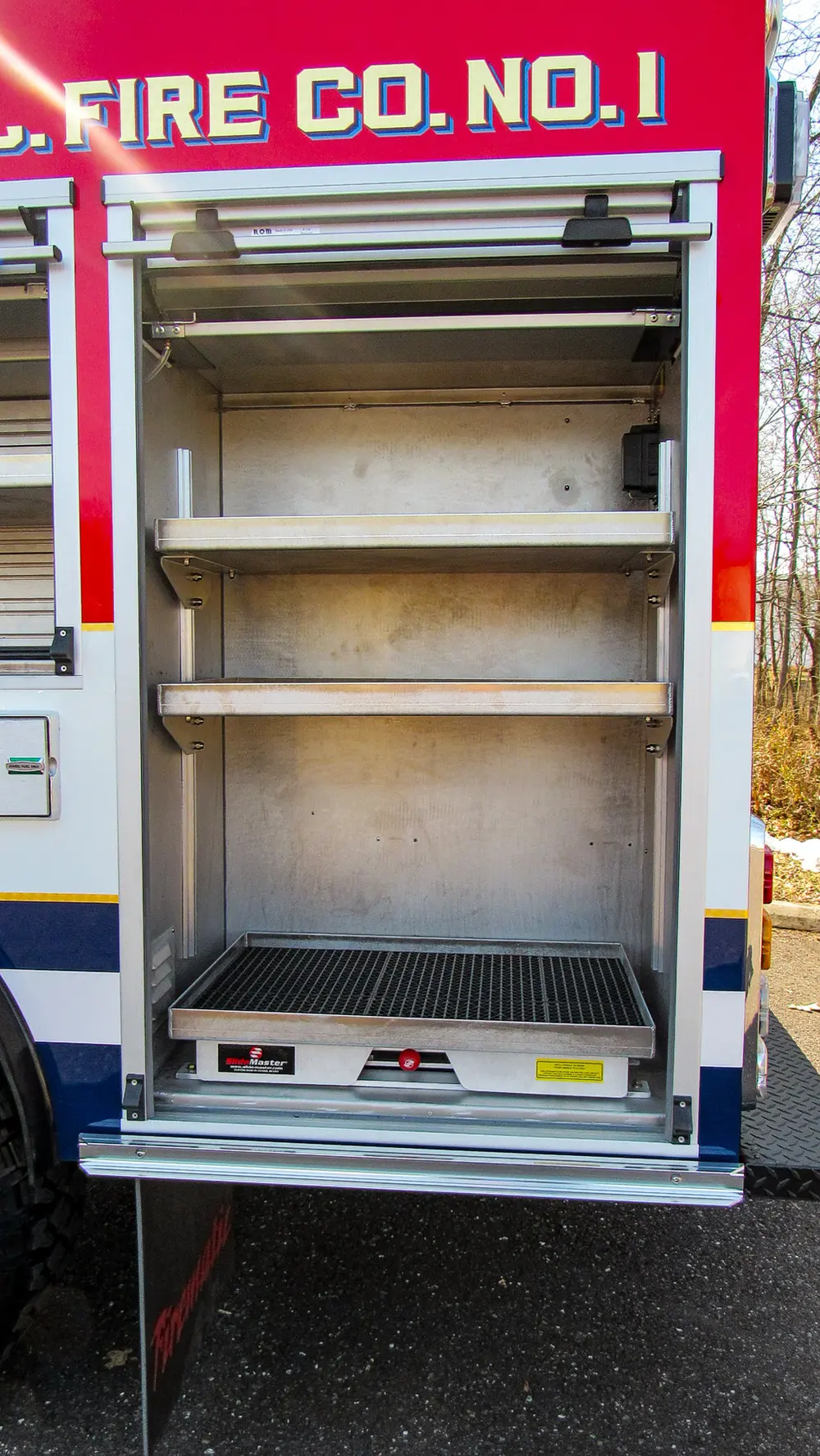 Exterior view of small fire truck showing cab, body compartments, and wheel/tire area.