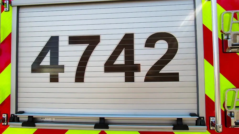 Exterior view of small fire truck showing cab, body compartments, and wheel/tire area.