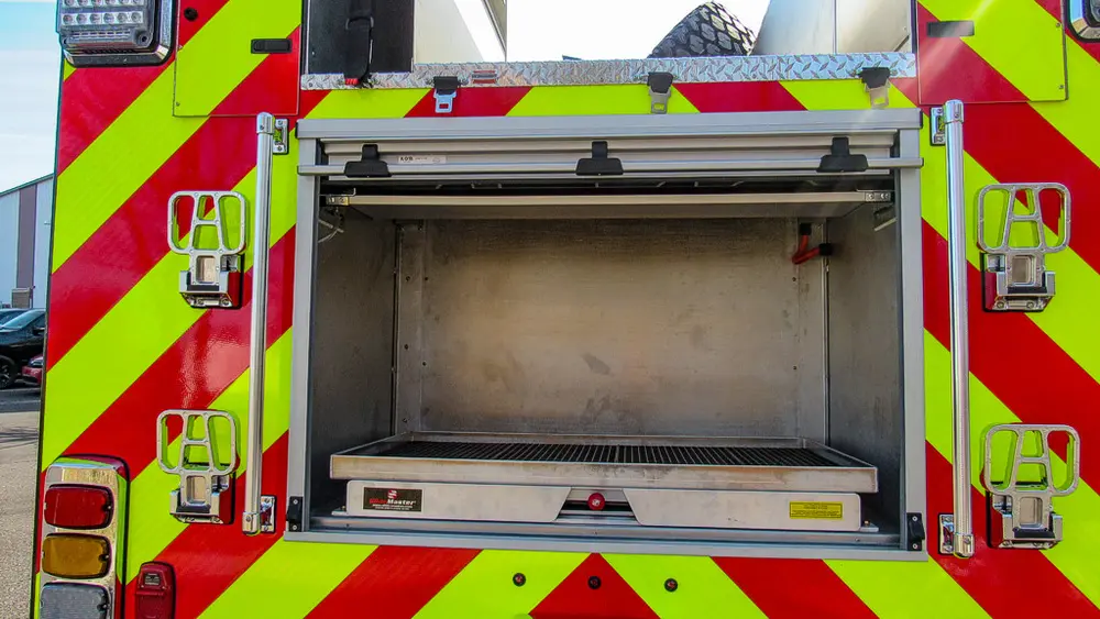 Exterior view of small fire truck showing cab, body compartments, and wheel/tire area.