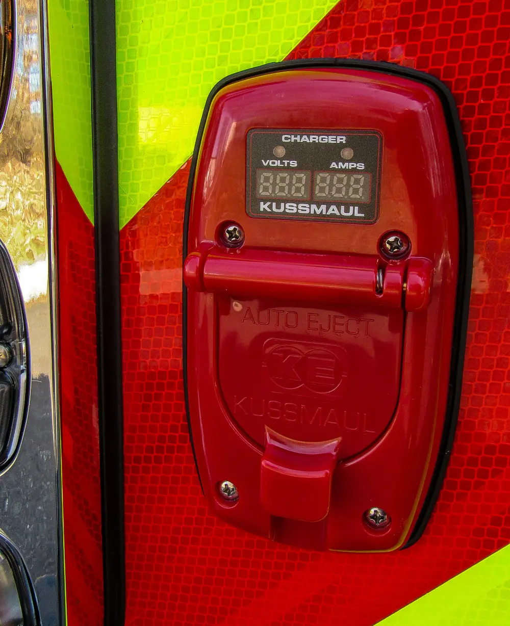 Exterior view of small fire truck showing cab, body compartments, and wheel/tire area.