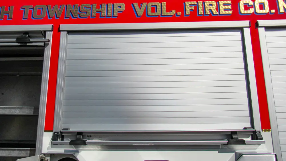 Exterior view of small fire truck showing cab, body compartments, and wheel/tire area.