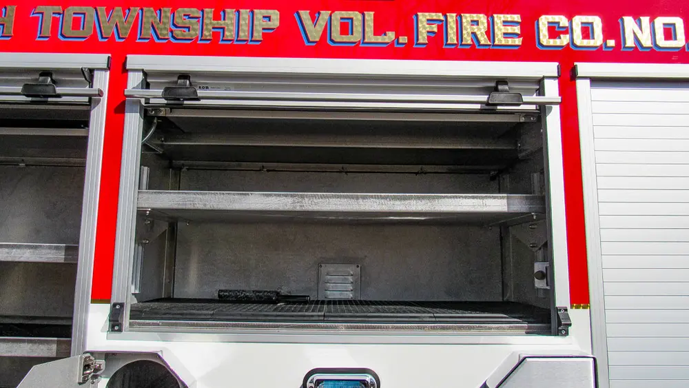 Exterior view of small fire truck showing cab, body compartments, and wheel/tire area.