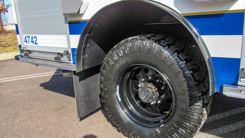 Exterior view of small fire truck showing cab, body compartments, and wheel/tire area.
