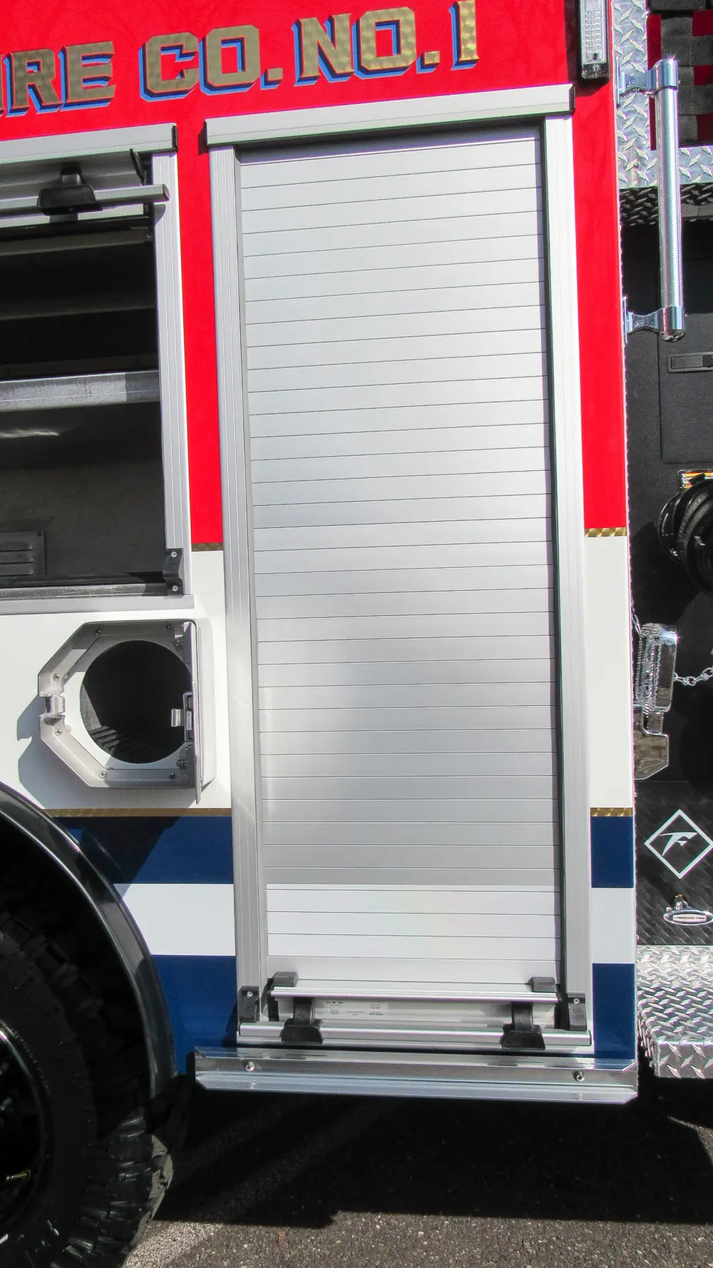 Exterior view of small fire truck showing cab, body compartments, and wheel/tire area.