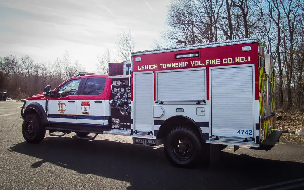 Exterior view of small fire truck showing cab, body compartments, and wheel/tire area.