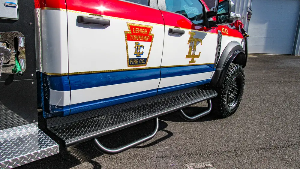 Exterior view of small fire truck showing cab, body compartments, and wheel/tire area.