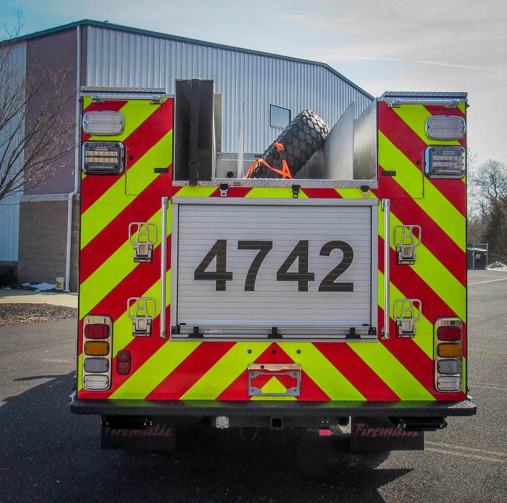 Exterior view of small fire truck showing cab, body compartments, and wheel/tire area.