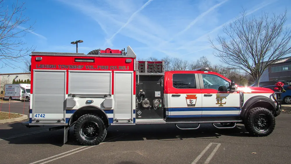 Exterior view of small fire truck showing cab, body compartments, and wheel/tire area.