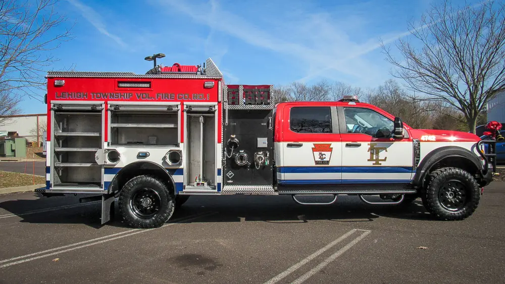 Exterior view of small fire truck showing cab, body compartments, and wheel/tire area.