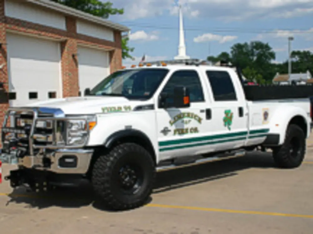 Exterior view of small fire truck showing cab, body compartments, and wheel/tire area.