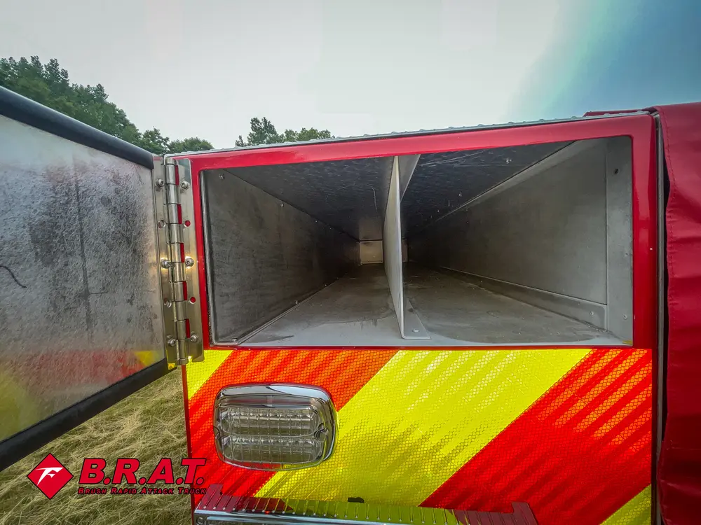 Exterior view of small fire truck showing cab, body compartments, and wheel/tire area.
