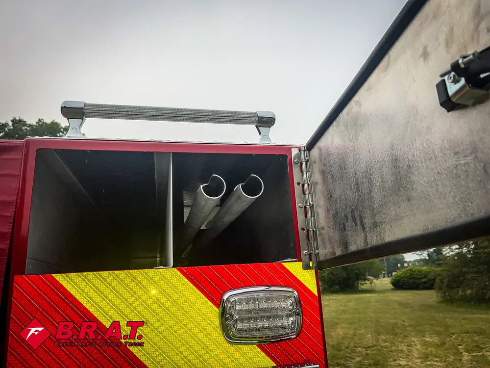 Exterior view of small fire truck showing cab, body compartments, and wheel/tire area.