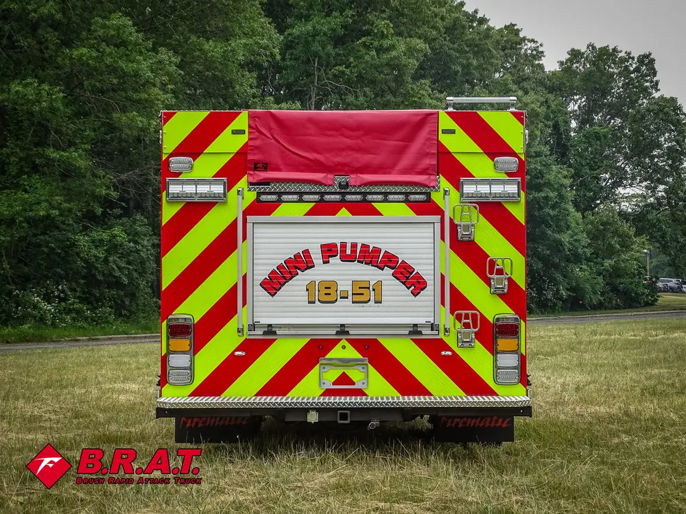 Exterior view of small fire truck showing cab, body compartments, and wheel/tire area.