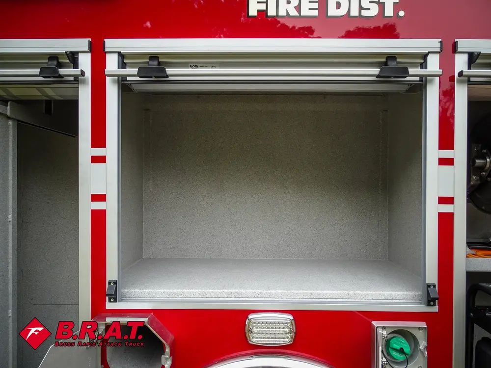 Exterior view of small fire truck showing cab, body compartments, and wheel/tire area.