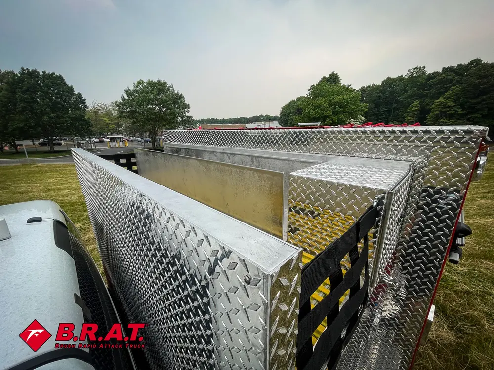Exterior view of small fire truck showing cab, body compartments, and wheel/tire area.