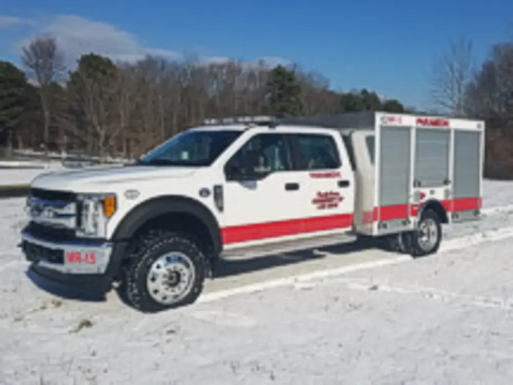 Exterior view of small fire truck showing cab, body compartments, and wheel/tire area.
