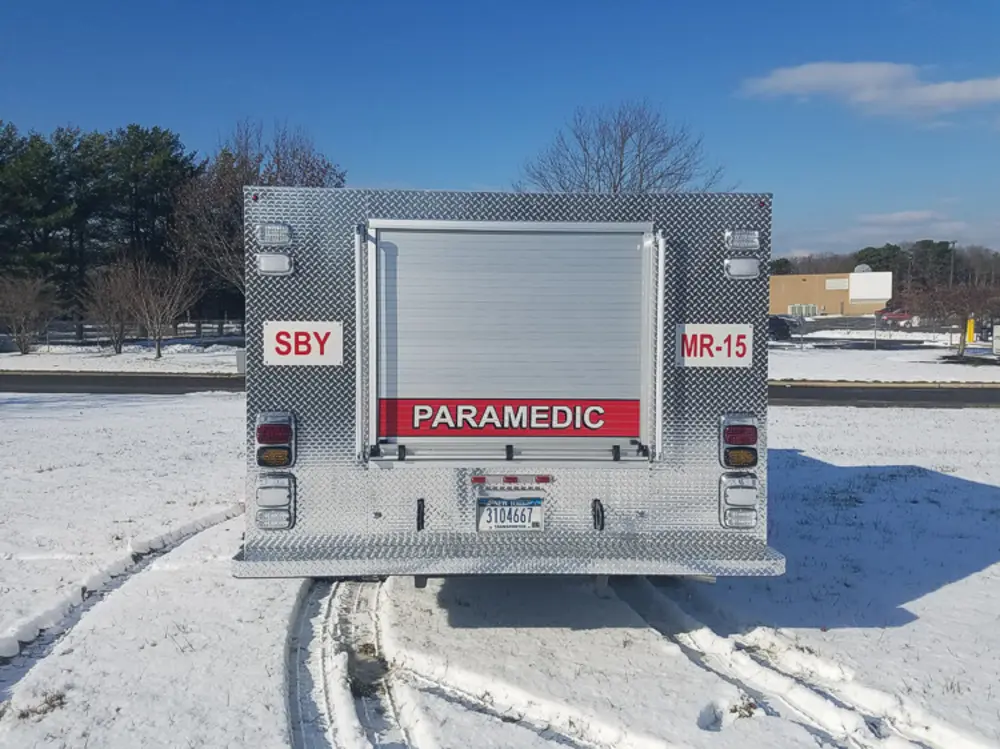 Exterior view of small fire truck showing cab, body compartments, and wheel/tire area.