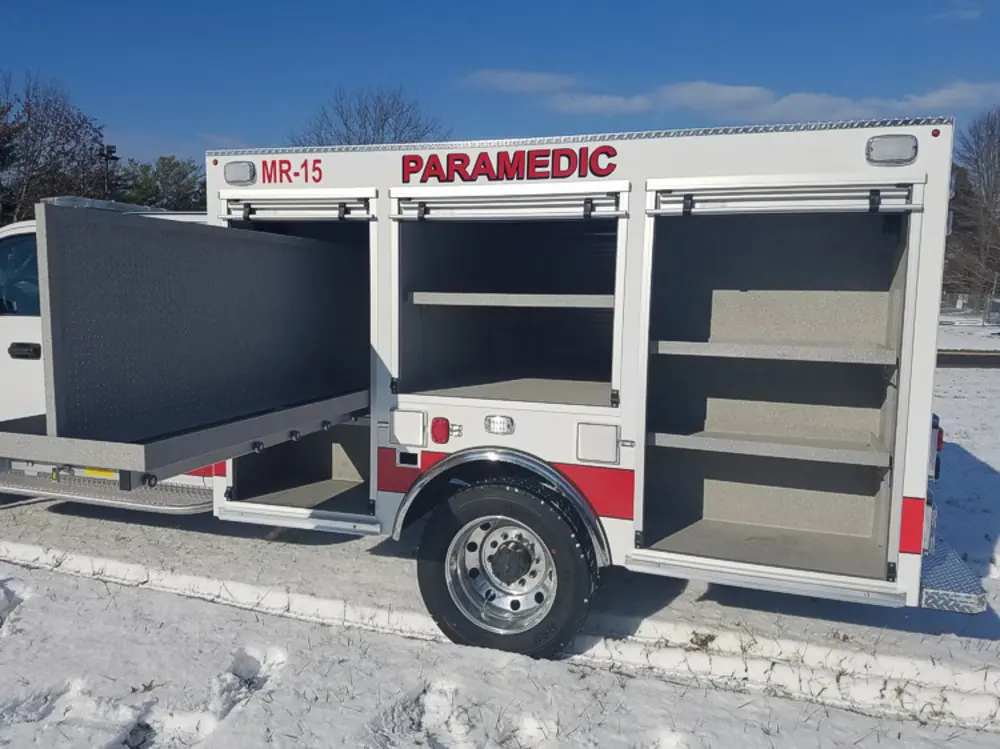 Exterior view of small fire truck showing cab, body compartments, and wheel/tire area.