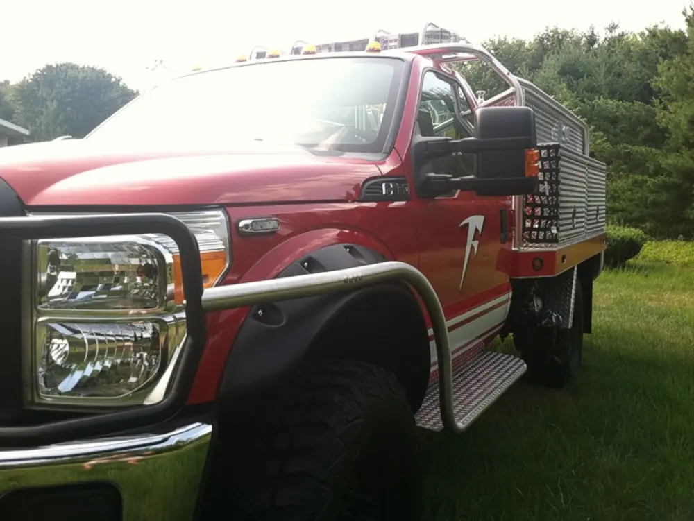Exterior view of small fire truck showing cab, body compartments, and wheel/tire area.