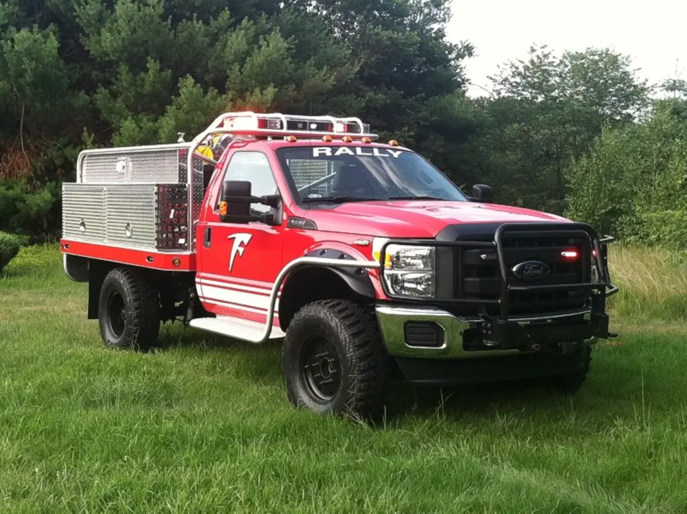 Exterior view of small fire truck showing cab, body compartments, and wheel/tire area.