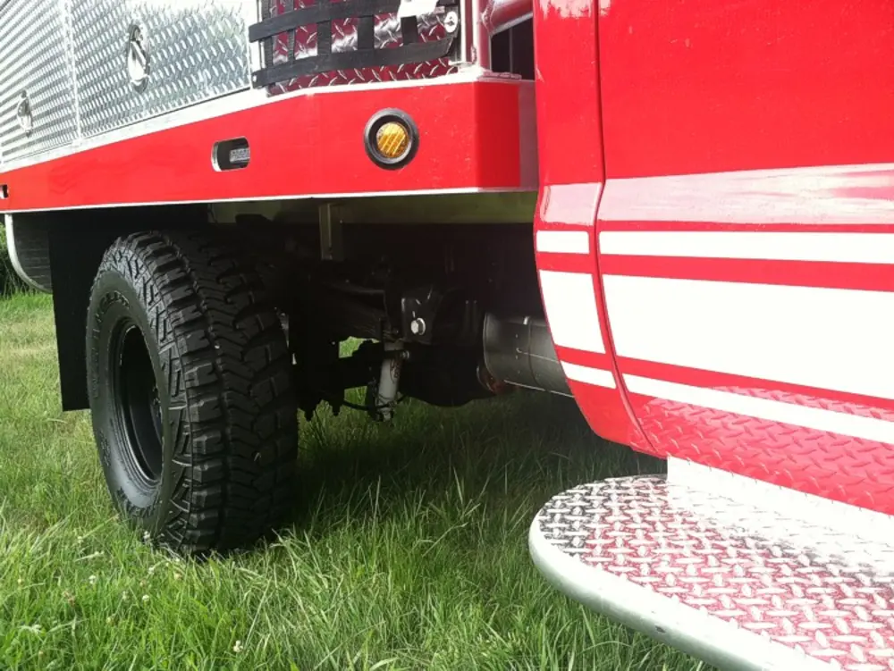 Exterior view of small fire truck showing cab, body compartments, and wheel/tire area.