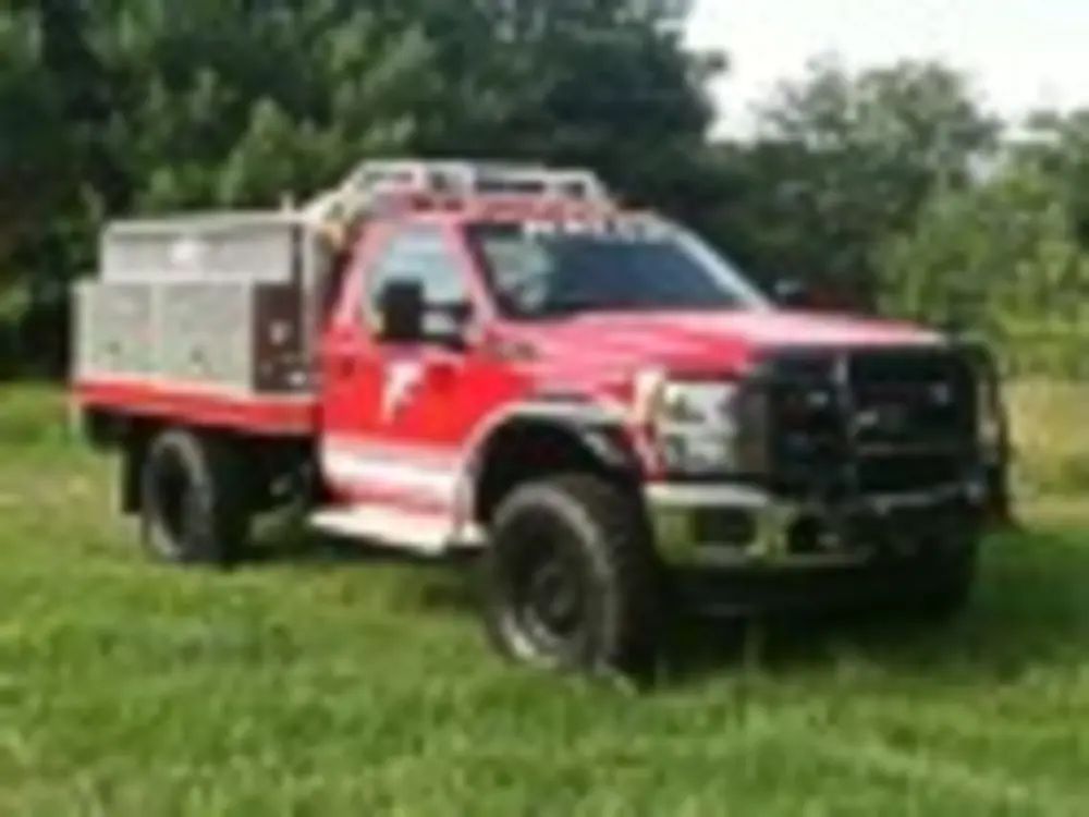 Exterior view of small fire truck showing cab, body compartments, and wheel/tire area.