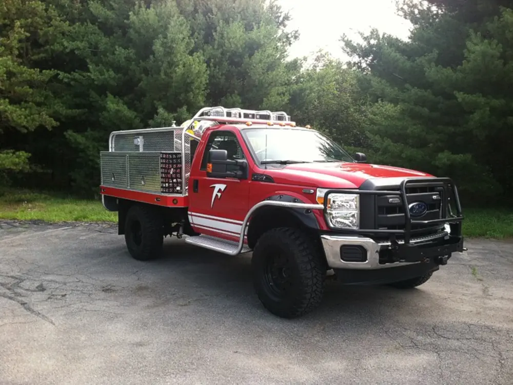 Exterior view of small fire truck showing cab, body compartments, and wheel/tire area.