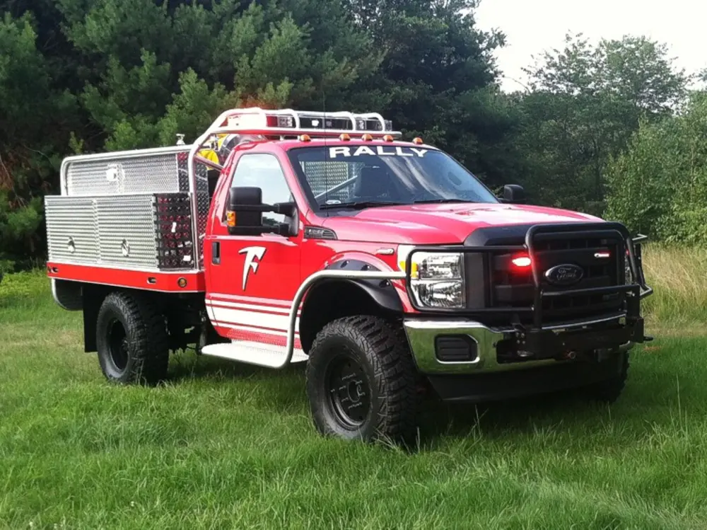 Exterior view of small fire truck showing cab, body compartments, and wheel/tire area.