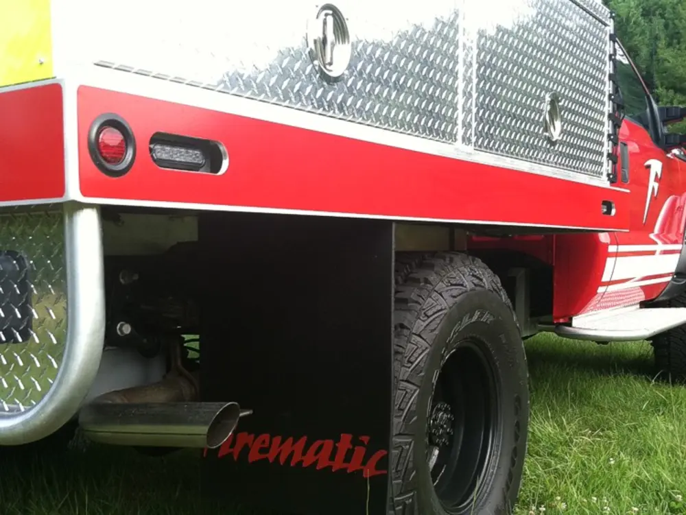 Exterior view of small fire truck showing cab, body compartments, and wheel/tire area.