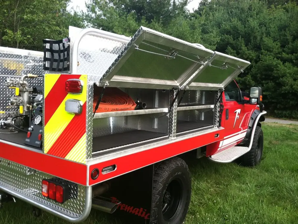 Exterior view of small fire truck showing cab, body compartments, and wheel/tire area.