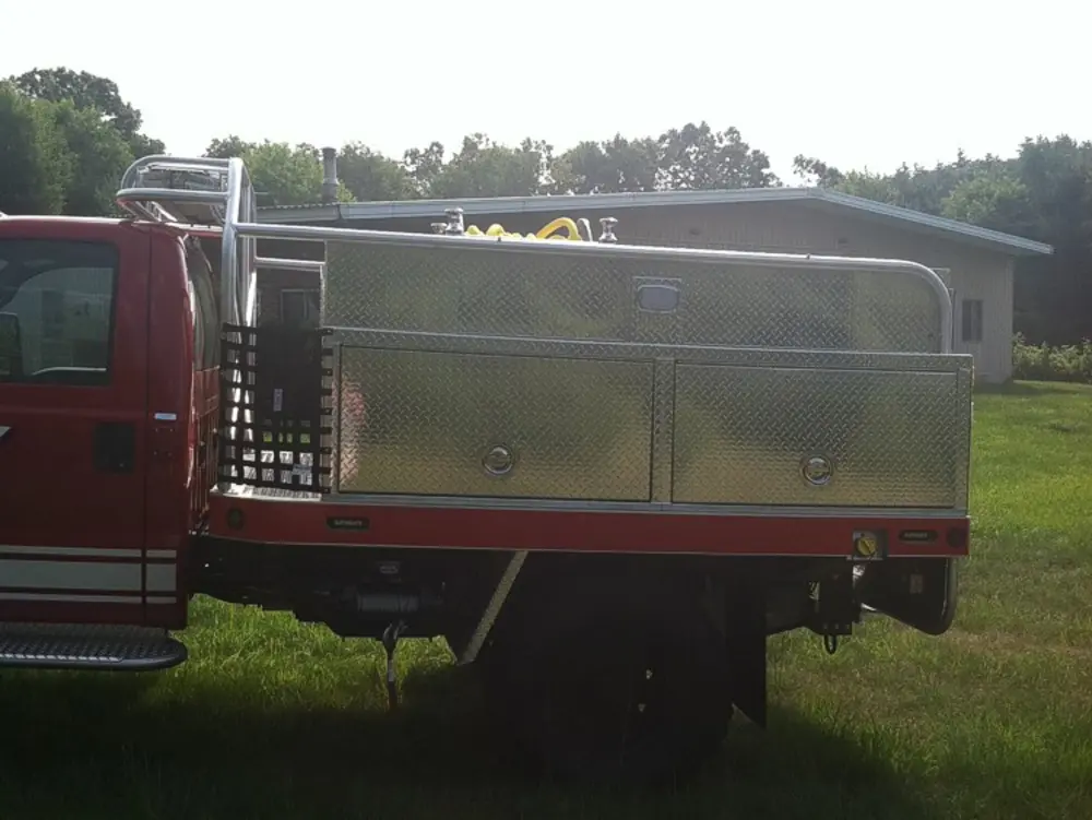 Exterior view of small fire truck showing cab, body compartments, and wheel/tire area.