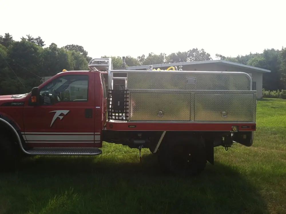Exterior view of small fire truck showing cab, body compartments, and wheel/tire area.