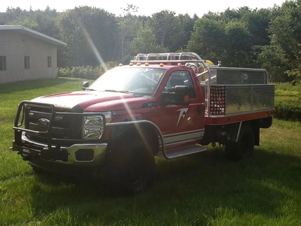 Exterior view of small fire truck showing cab, body compartments, and wheel/tire area.