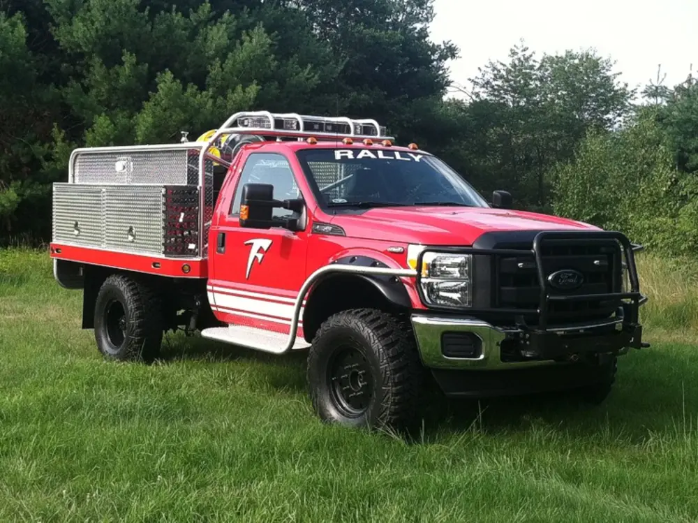 Exterior view of small fire truck showing cab, body compartments, and wheel/tire area.