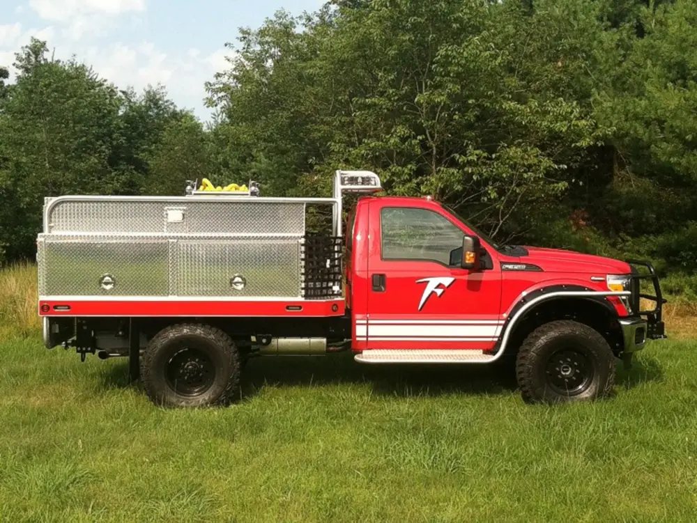 Exterior view of small fire truck showing cab, body compartments, and wheel/tire area.