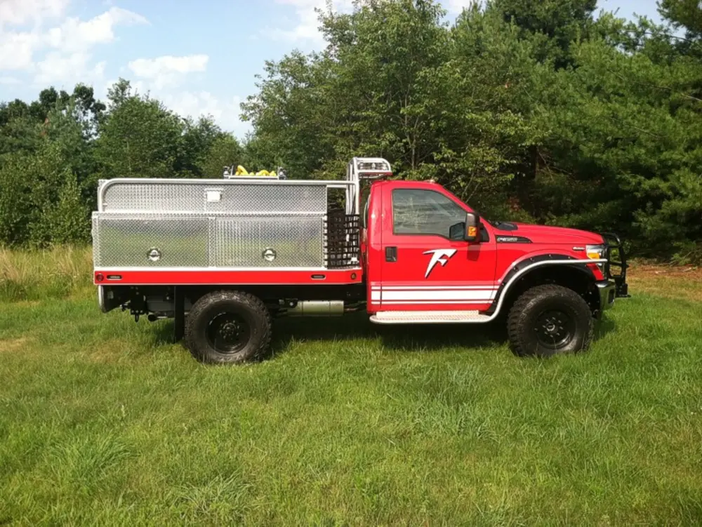 Exterior view of small fire truck showing cab, body compartments, and wheel/tire area.