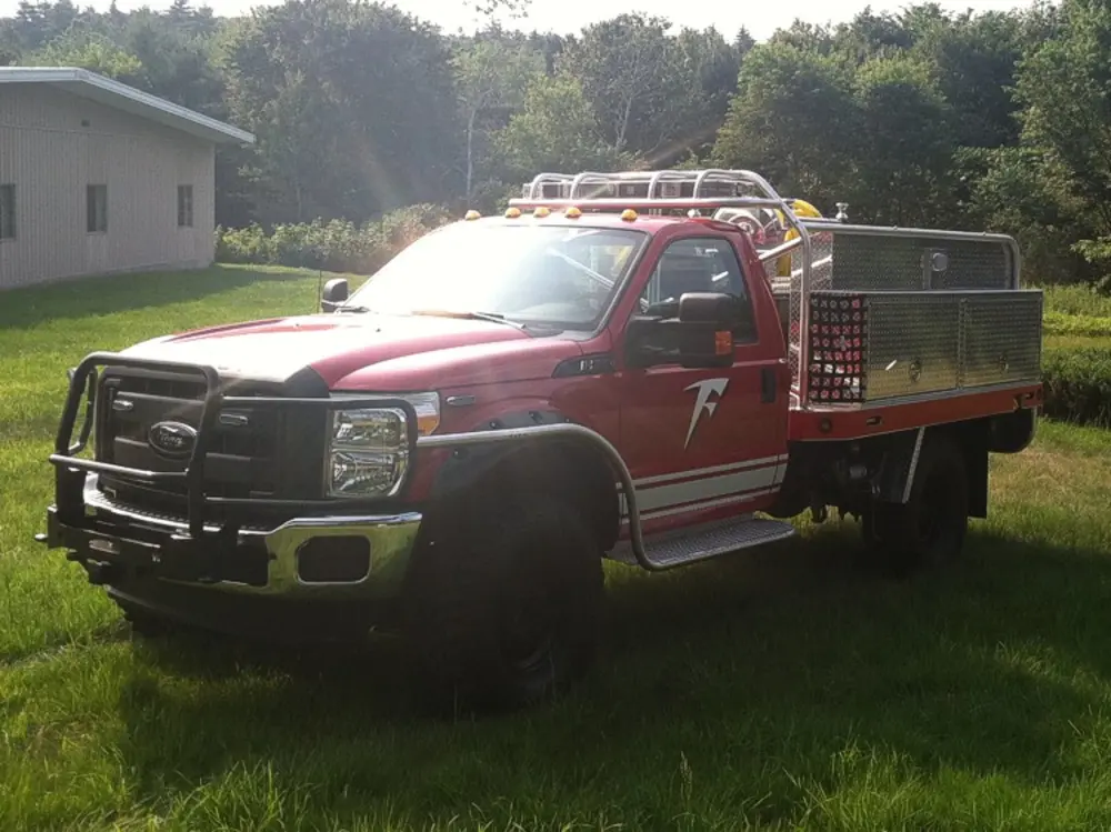 Exterior view of small fire truck showing cab, body compartments, and wheel/tire area.