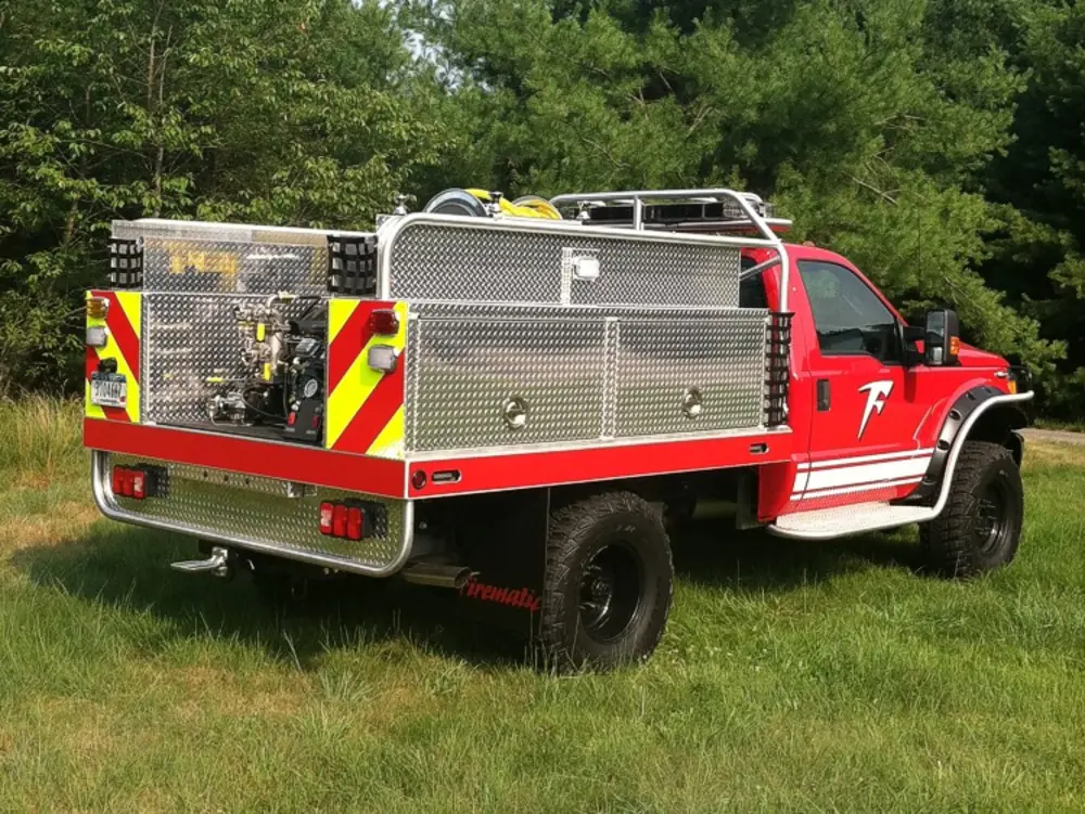 Exterior view of small fire truck showing cab, body compartments, and wheel/tire area.