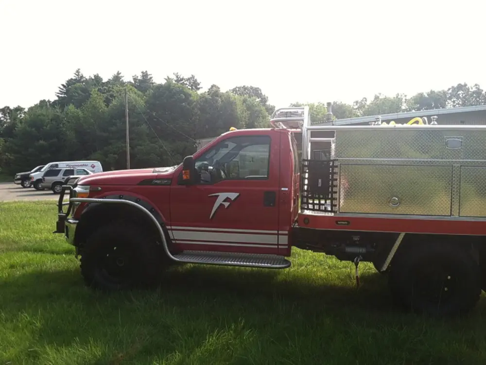 Exterior view of small fire truck showing cab, body compartments, and wheel/tire area.