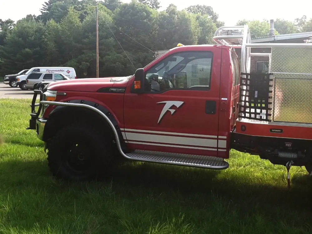 Exterior view of small fire truck showing cab, body compartments, and wheel/tire area.