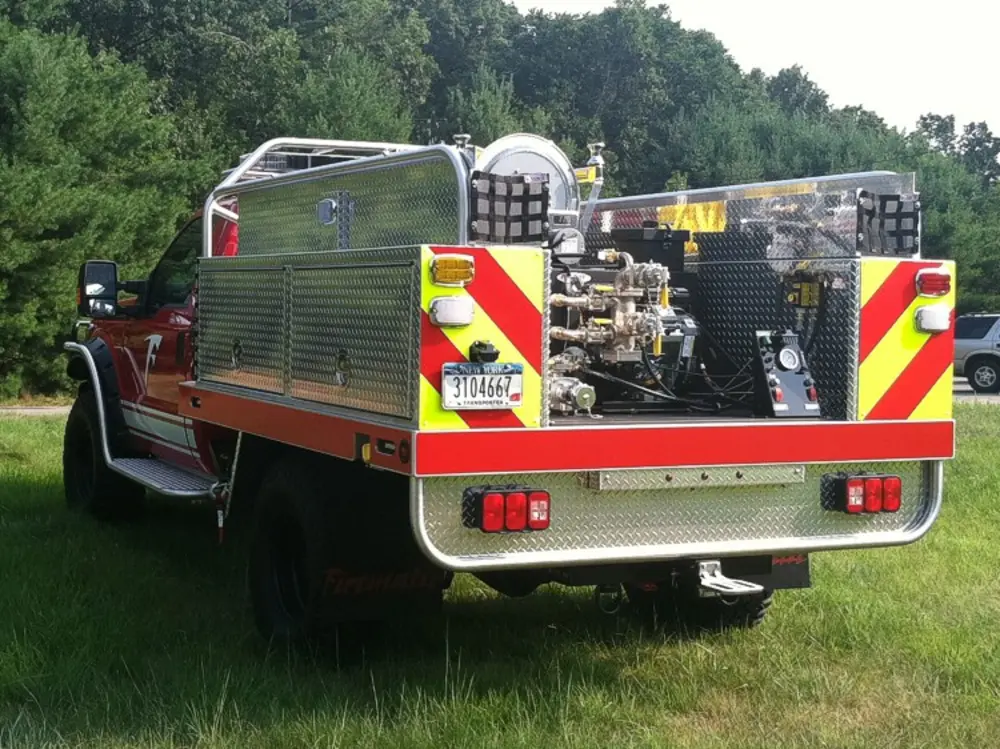 Exterior view of small fire truck showing cab, body compartments, and wheel/tire area.