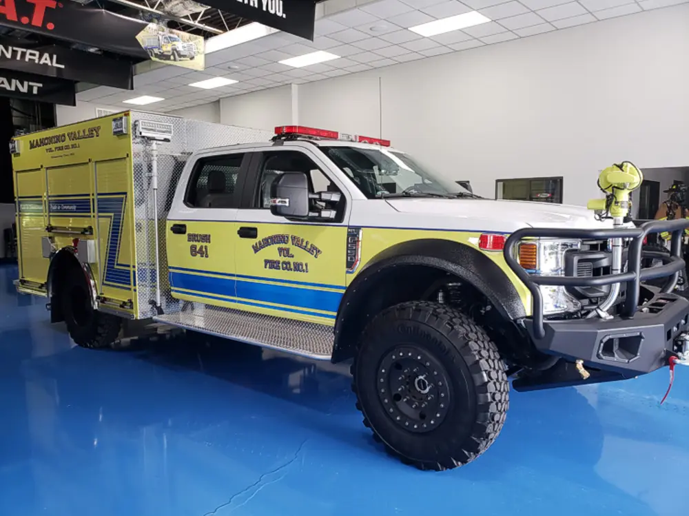 Exterior view of small fire truck showing cab, body compartments, and wheel/tire area.