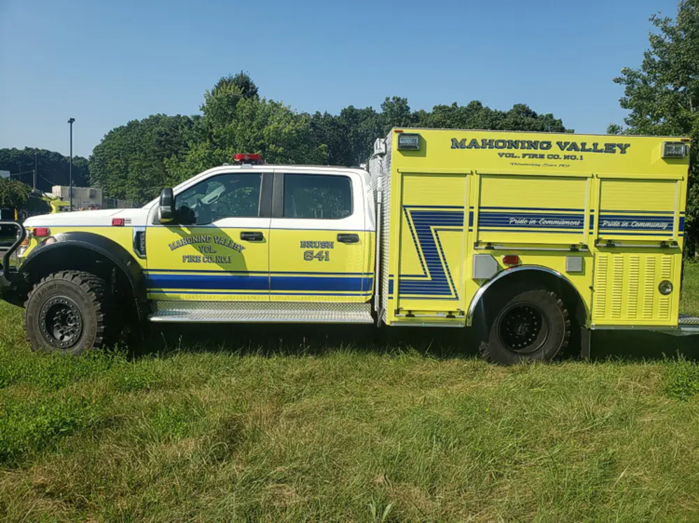Exterior view of small fire truck showing cab, body compartments, and wheel/tire area.