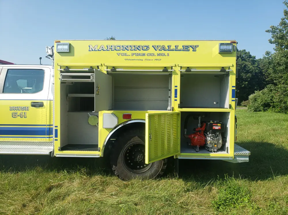 Exterior view of small fire truck showing cab, body compartments, and wheel/tire area.