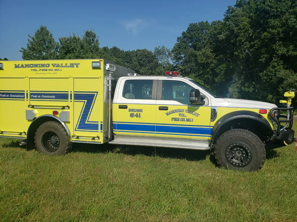 Exterior view of small fire truck showing cab, body compartments, and wheel/tire area.