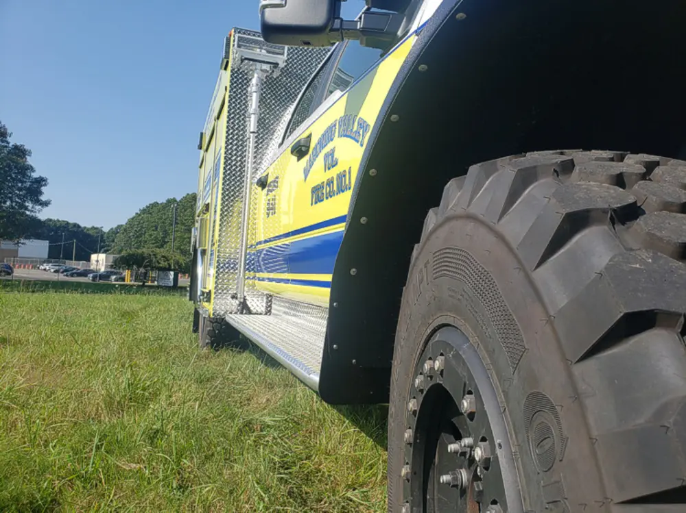 Exterior view of small fire truck showing cab, body compartments, and wheel/tire area.