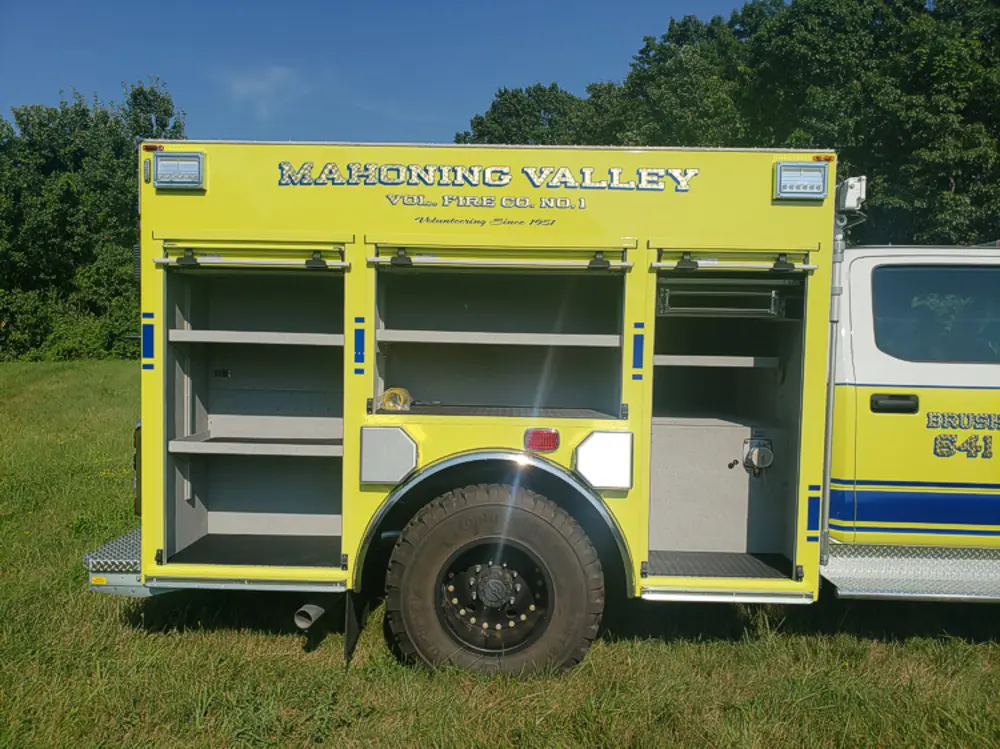 Exterior view of small fire truck showing cab, body compartments, and wheel/tire area.