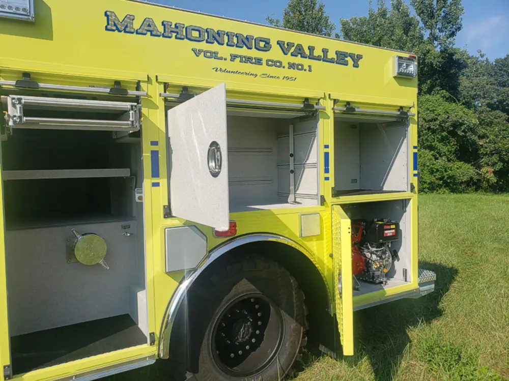 Exterior view of small fire truck showing cab, body compartments, and wheel/tire area.