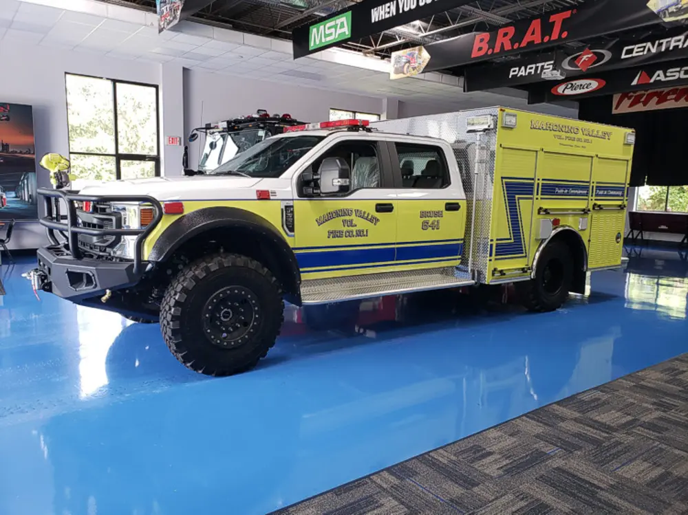 Exterior view of small fire truck showing cab, body compartments, and wheel/tire area.