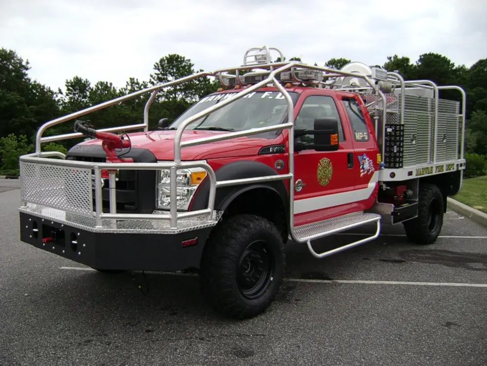 Exterior view of small fire truck showing cab, body compartments, and wheel/tire area.